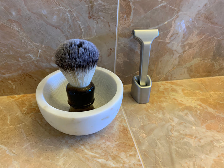 The Single Edge Razor standing tall on the Supply Razor Stand beside the Synthetic Shaving Brush lying inside the Marble Bowl