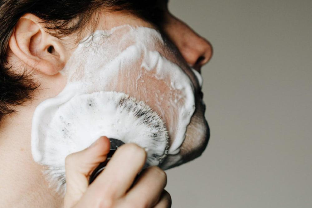 A man applying the shave cream using a shaving brush