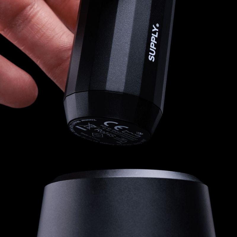 Close-up of a Supply-branded electric trimmer being placed on its charging dock against a black background