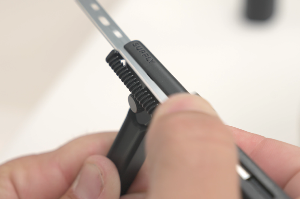 Close-up of hands adjusting a Supply-branded razor with a precision blade against a blurred background