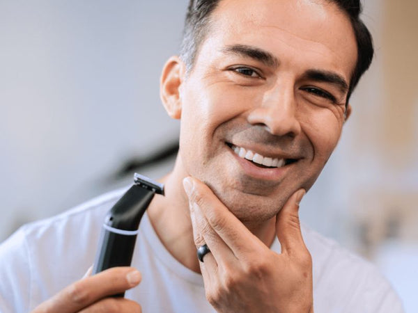 Smiling man using an electric beard trimmer while grooming his facial hair